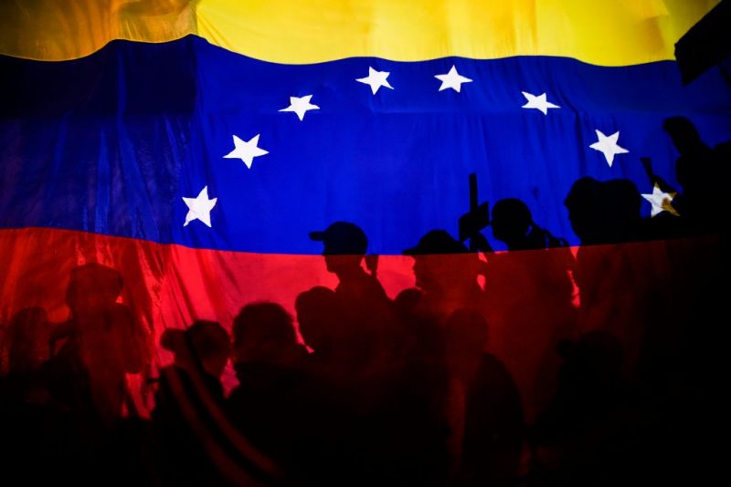 TOPSHOT - Opposition activists, seen here behind a Venezuelan flag, protest against the deaths of 43 people in clashes with the police during weeks of demonstrations against the government of Venezuelan President Nicolas Maduro, in Caracas on May 17, 2017. - The United States warned on Wednesday at the United Nations that Venezuela's crisis was worsening and could escalate into a major conflict similar to Syria or South Sudan. (Photo by JUAN BARRETO / AFP) (Photo by JUAN BARRETO/AFP via Getty Images)