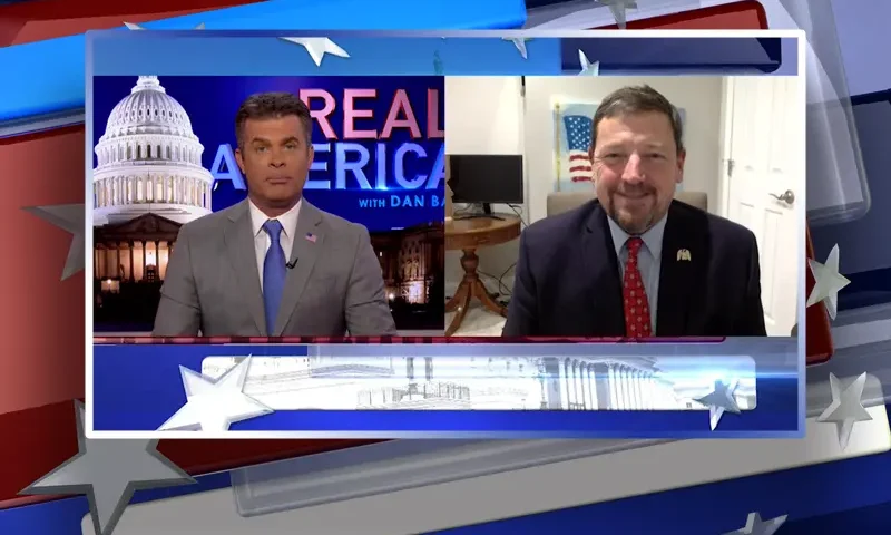 Video still from Real America on One America News Network showing a split screen of the host on the left side, and on the right side is the guest, Ed Martin.