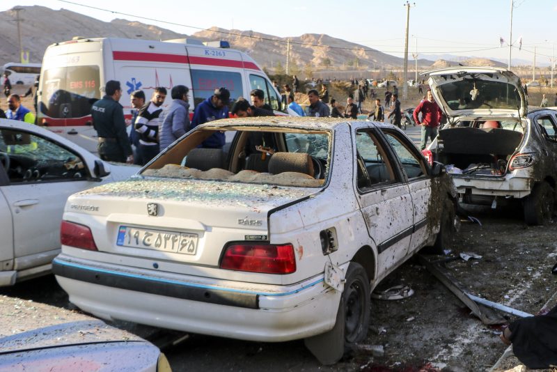 People stay next to destroyed cars after an explosion in Kerman, Iran, Wednesday, Jan. 3, 2024. Iran says bomb blasts at an event honoring a prominent Iranian general slain in a U.S. airstrike in 2020 have killed at least 103 people and wounded 188 others. (Tasnim News Agency via AP)