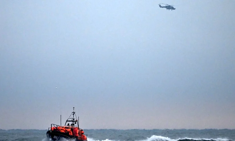 TOPSHOT-BRITAIN-FRANCE-EU-MIGRATION TOPSHOT - Migrants, picked up at sea attempting to cross the English Channel from France, are brought ashore on a Royal National Lifeboat Institution (RNLI) lifeboat, as a Maritime and Coastguard Agency (MCA) helicopter patrols in the distance, at Dungeness on the southeast coast of England, on December 9, 2022. (Photo by Ben Stansall / AFP) (Photo by BEN STANSALL/AFP via Getty Images)