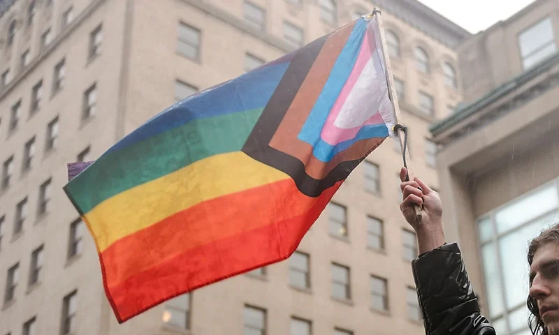 A speaker waves a Progress Pride Flag as LGBTQ activists protest on March 17, 2023, in front of the US Consulate in Montreal, Canada, calling for transgender and non-binary people be admitted into Canada. - According to police services, some 200 people gathered in the rain to show support for the trans community in the United States. (Photo by ANDREJ IVANOV / AFP) (Photo by ANDREJ IVANOV/AFP via Getty Images)