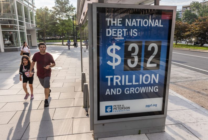 WASHINGTON, DC - JULY 05: Pedestrians walk past a bus shelter at Pennsylvania Avenue and 22nd Street NW where an electronic billboard and a poster display the current U.S. National debt per person and as a nation at 32 Trillion dollars on July 05, 2023 in Washington, DC. (Photo by Jemal Countess/Getty Images for the Peter G. Peterson Foundation)