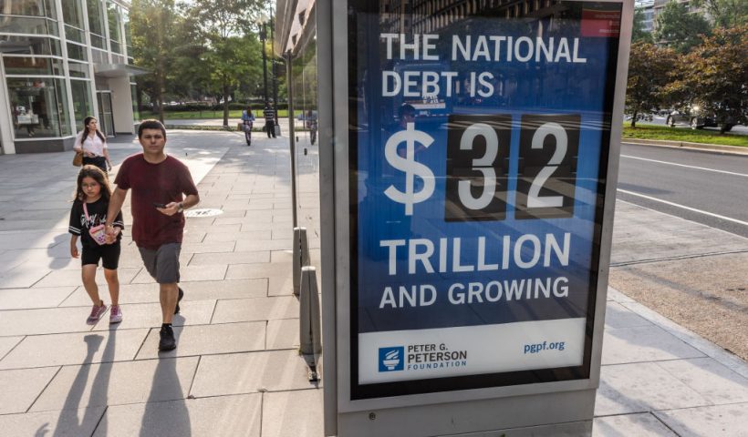 WASHINGTON, DC - JULY 05: Pedestrians walk past a bus shelter at Pennsylvania Avenue and 22nd Street NW where an electronic billboard and a poster display the current U.S. National debt per person and as a nation at 32 Trillion dollars on July 05, 2023 in Washington, DC. (Photo by Jemal Countess/Getty Images for the Peter G. Peterson Foundation)