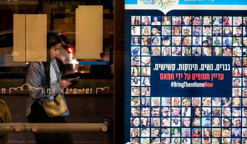 TOPSHOT - A woman stands at a bus stop in Tel Aviv near a combination of photos and a sign calling for the release of hostages held in the Gaza Strip by Hamas militants, on November 21, 2023 in Tel Aviv, amid ongoing battles between Israel and the Palestinian armed group. Israeli Prime Minister Benjamin Netanyahu said on November 21, that "we are making progress" on the return of hostages Hamas seized during the October 7 attacks, after mediators said a truce deal was in sight. (Photo by AHMAD GHARABLI / AFP) (Photo by AHMAD GHARABLI/AFP via Getty Images)
