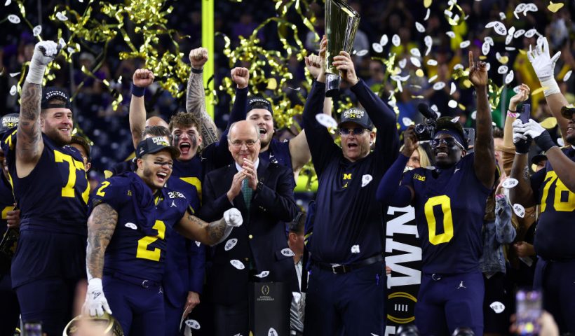 HOUSTON, TEXAS - JANUARY 08: Head coach Jim Harbaugh of the Michigan Wolverines and his team react as he lifts the national championship trophy after defeating the Washington Huskies during the 2024 CFP National Championship game at NRG Stadium on January 08, 2024 in Houston, Texas. Michigan defeated Washington 34-13. (Photo by Maddie Meyer/Getty Images)