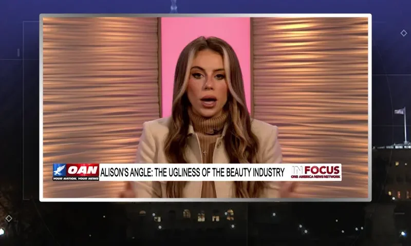 Video still of the host of In Focus at the desk of their talk show on One America News Network.