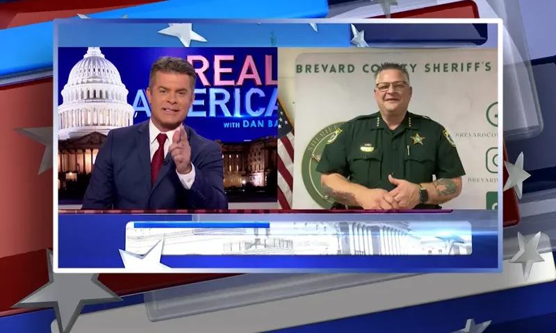 Video still from Real America on One America News Network showing a split screen of the host on the left side, and on the right side is the guest, Sheriff Wayne Ivey.