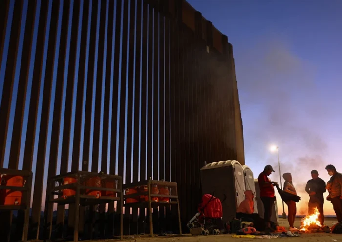 YUMA, ARIZONA - MAY 22: Immigrants from Cuba and Venezuela warm themselves by a fire before sunrise along the U.S.-Mexico border barrier as they await processing by the U.S. Border Patrol after crossing from Mexico on May 22, 2022 in Yuma, Arizona. Title 42, the controversial pandemic-era border policy enacted by former President Trump, which cites COVID-19 as the reason to rapidly expel asylum seekers at the U.S. border, was set to officially expire on May 23rd. A federal judge in Louisiana delivered a ruling May 20th blocking the Biden administration from lifting Title 42. (Photo by Mario Tama/Getty Images)