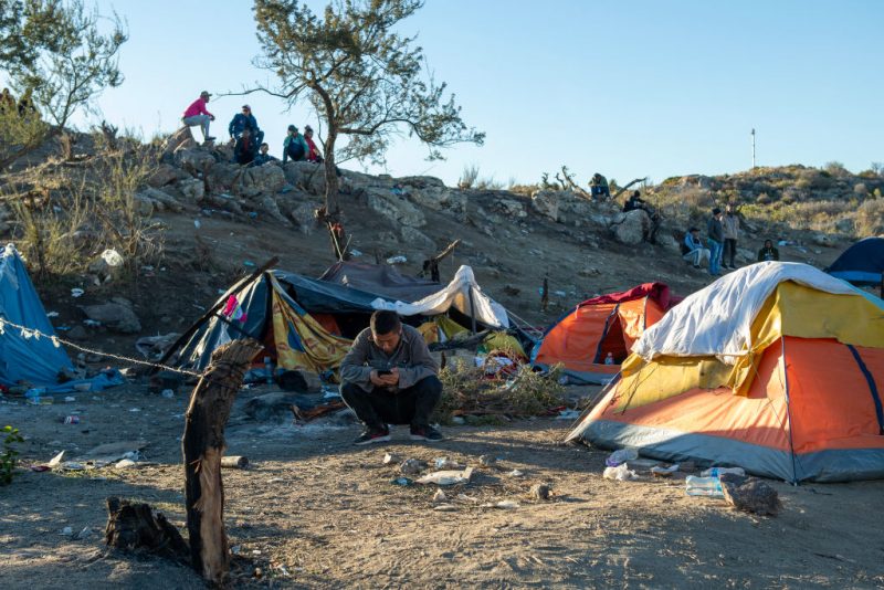 A Chinese migrant sit in front of his tent near the US-Mexico border fence in Jacumba, California, on December 6, 2023. Hundreds of migrants who cross into the United States each day are being herded into open-air camps, where they have no access to food or water, with some are left to sleep on the open ground in a desert riddled with scorpions and snakes, activists say. (Photo by VALERIE MACON / AFP) (Photo by VALERIE MACON/AFP via Getty Images)