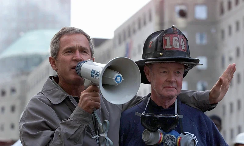 US President George W. Bush (L), standing next to NEW YORK, NY - SEPTEMBER 14: US President George W. Bush (L), standing next to retired firefighter Bob Beckwith, 69, speaks to volunteers and firemen as he surveys the damage at the site of the World Trade Center in New York in this 14 September 2001 file photo. Bush was presented with the same bullhorn he used to address the rescue workers in this photo at a ceremony 25 February 2002 in the Oval Office of the White House in Washington, DC which was attended by Beckwith and New York Governor George Pataki. The President said the bullhorn would be put on display at his father's Presidential Library. (Photo credit should read PAUL RICHARDS/AFP via Getty Images)