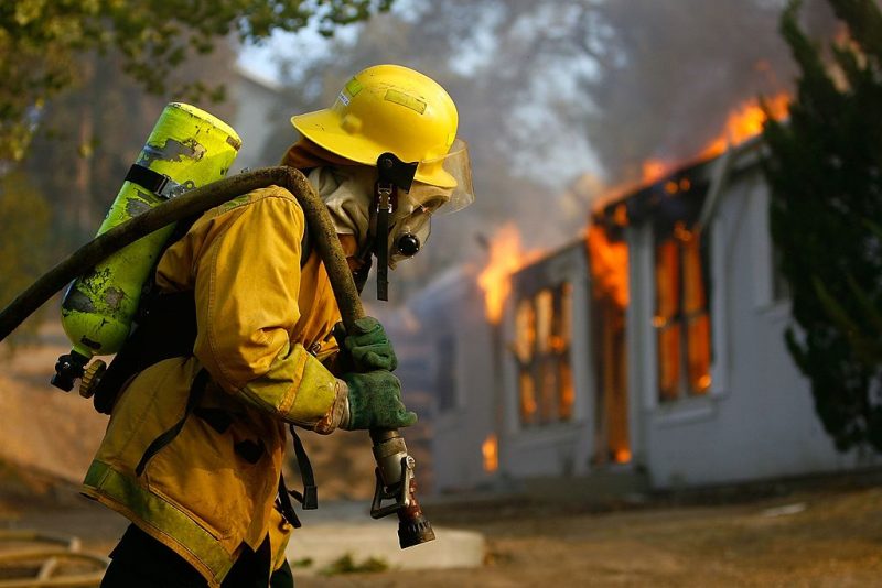 JAMUL, CA - OCTOBER 24: A US forestry firefighter pulls a hose to a burning home in Deerhorn Valley as the Harris Fire continues growing beyond 70,000 acres on October 24, 2007 near Jamul, California. Southern California is being ravaged by numerous record wildfires as Santa Ana Wind conditions push them into communities surrounded by native Chaparral habitat that has been dried by the driest rain season since records began 130 years ago. The fires are shaping up to be the worst wildfire event in San Diego County history. As many as 500,000 people have been evacuated from their homes. (Photo by David McNew/Getty Images)