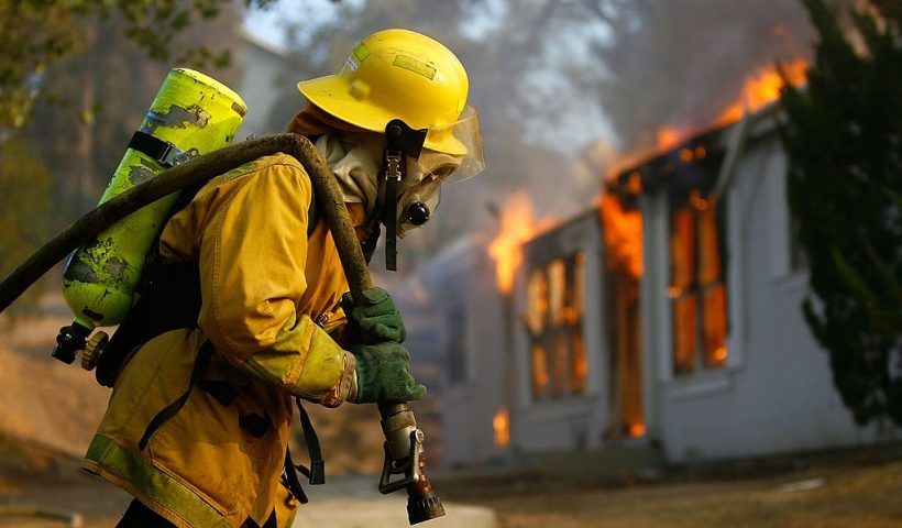 JAMUL, CA - OCTOBER 24: A US forestry firefighter pulls a hose to a burning home in Deerhorn Valley as the Harris Fire continues growing beyond 70,000 acres on October 24, 2007 near Jamul, California. Southern California is being ravaged by numerous record wildfires as Santa Ana Wind conditions push them into communities surrounded by native Chaparral habitat that has been dried by the driest rain season since records began 130 years ago. The fires are shaping up to be the worst wildfire event in San Diego County history. As many as 500,000 people have been evacuated from their homes. (Photo by David McNew/Getty Images)