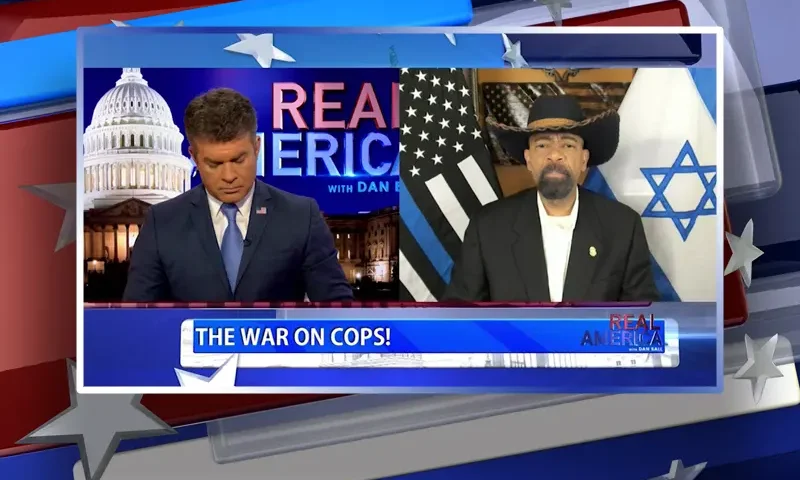 Video still from Real America on One America News Network showing a split screen of the host on the left side, and on the right side is the guest, Sheriff David Clarke.