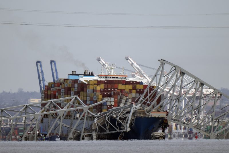 A container ship rests against wreckage of the Francis Scott Key Bridge on Tuesday, March 26, 2024, as seen from Pasadena, Md. The ship rammed into the major bridge in Baltimore early Tuesday, causing it to collapse in a matter of seconds and creating a terrifying scene as several vehicles plunged into the chilly river below. (AP Photo/Mark Schiefelbein)