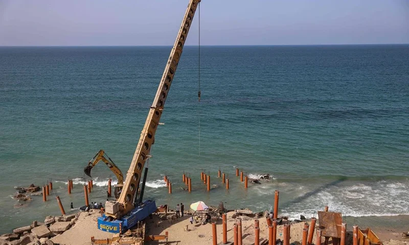 A crane is used to deploy stilts for the construction of a new pier and restaurant building along the Mediterranean seashore in Gaza City on October 27, 2021. - Posters of Egyptian President Abdel Fattah al-Sisi beam out over a site in the war-battered Gaza Strip where labourers and bulldozers are hard at work rebuilding. After years of retreat, Egypt is making its presence felt again in the neighbouring Palestinian enclave, emerging as a key benefactor in the aftermath of the last bout of fighting between Hamas and Israel in May. (Photo by MOHAMMED ABED / AFP) (Photo by MOHAMMED ABED/AFP via Getty Images)