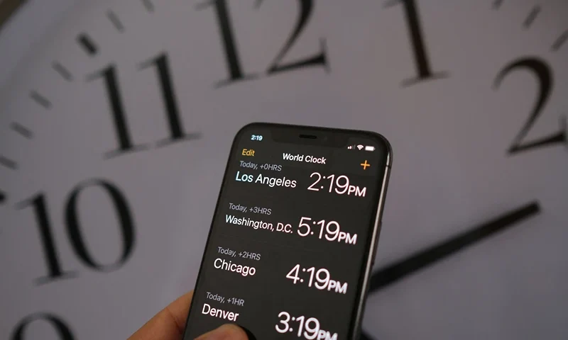 This illustration photo shows a clock in the background of a smartphone showing the time after daylight saving time was implemented in Los Angeles, California, on March 15, 2022. The US Senate advanced a bill on March 15 that would bring an end to the twice-yearly changing of clocks, in favor of a "new, permanent standard time" that would mean brighter winter evenings. (Photo by Chris DELMAS / AFP) (Photo by CHRIS DELMAS/AFP via Getty Images)