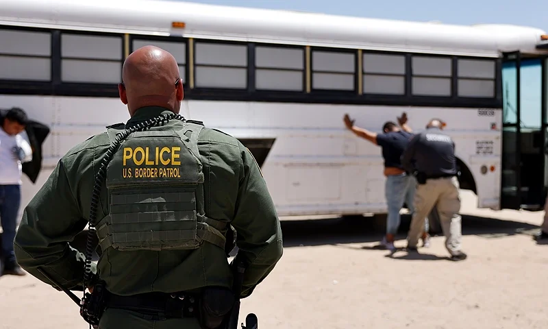 YUMA, ARIZONA - MAY 10: A U.S. Border Patrol agent keeps watch as immigrants seeking asylum are searched before boarding a bus to be processed after crossing into Arizona from Mexico on May 10, 2023 in Yuma, Arizona. A surge of immigrants is expected with the end of the U.S. government's Covid-era Title 42 policy, which for the past three years has allowed for the quick expulsion of irregular migrants entering the country. (Photo by Mario Tama/Getty Images)