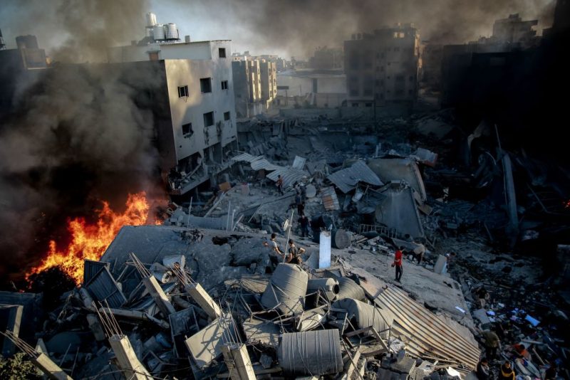 TOPSHOT - Smoke and fire rise from a levelled building as people gather amid the destruction in the aftermath of an Israeli strike on Gaza City on October 26, 2023, as battles continue between Israel and the Palestinian Hamas group. (Photo by Omar El-Qattaa / AFP) (Photo by OMAR EL-QATTAA/AFP via Getty Images)
