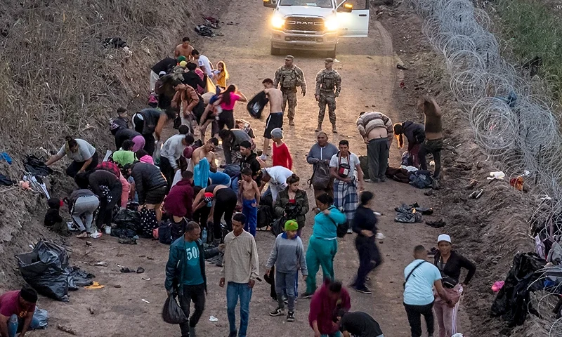 EAGLE PASS, TEXAS - DECEMBER 20: Seen from an aerial view, Texas National Guard troops look on as immigrants change into dry clothes after wading through the Rio Grande from Mexico early on December 20, 2023 in Eagle Pass, Texas. A late-year surge of migrants crossing the U.S. southern border has overwhelmed U.S. immigration officials. (Photo by John Moore/Getty Images)