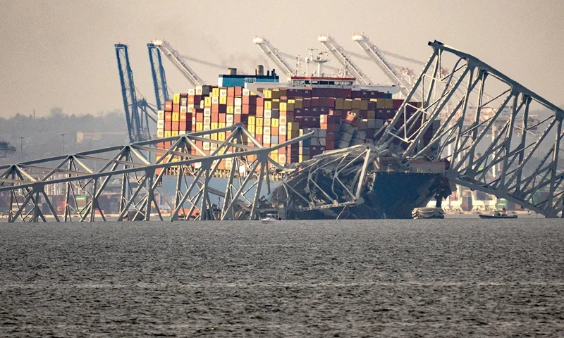 US-TRANSPORT-ACCIDENT-ECONOMY Part of the steel frame of the Francis Scott Key Bridge sits on top of the container ship Dali after the bridge collapsed in Baltimore, Maryland, on March 26, 2024. The bridge collapsed early March 26 after being struck by the Singapore-flagged Dali container ship, sending multiple vehicles and people plunging into the frigid harbor below. There was no immediate confirmation of the cause of the disaster, but Baltimore's Police Commissioner Richard Worley said there was "no indication" of terrorism. (Photo by Kent Nishimura / AFP) (Photo by KENT NISHIMURA/AFP via Getty Images)