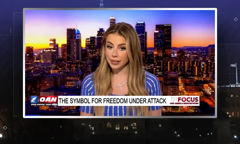 Video still of the host of In Focus at the desk of their talk show on One America News Network.