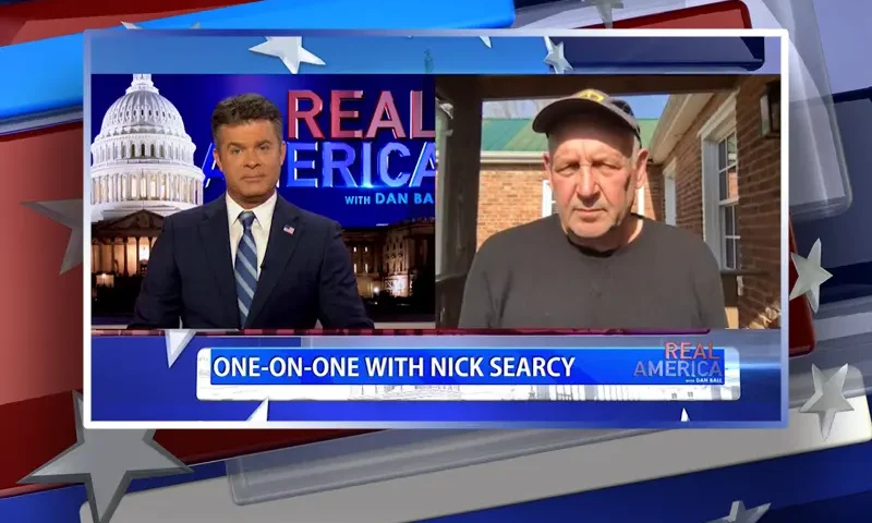 Video still from Real America on One America News Network showing a split screen of the host on the left side, and on the right side is the guest, Nick Searcy.