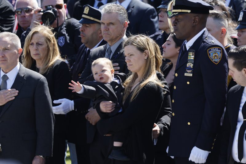 MASSAPEQUA, NEW YORK - MARCH 30: Stephanie Diller, the widow of NYPD officer Jonathan Diller, carries her son Ryan at the funeral of her husband at St. Rose of Lima R.C. Church on March 30, 2024 in Massapequa, New York. Officer Diller was killed on March 25th when he was shot in Queens after approaching an illegally parked vehicle. Two suspects have been arrested, charged and are being held and without bail for the murder of Diller. (Photo by Michael M. Santiago/Getty Images)