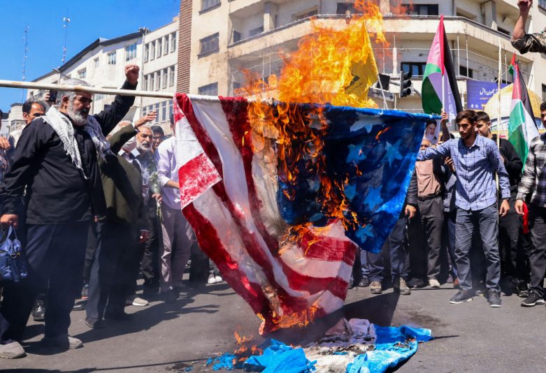TOPSHOT - Demonstrators burn a US and an Israeli flag during the funeral for seven Islamic Revolutionary Guard Corps members killed in a strike in Syria, which Iran blamed on Israel, in Tehran on April 5, 2024. The Guards, including two generals, were killed in the air strike on April 1, which levelled the Iranian embassy's consular annex in Damascus. The funeral ceremony coincides with the annual Quds (Jerusalem) Day commemorations, when Iran and its allies stage marches in support of the Palestinians. (Photo by Atta KENARE / AFP) (Photo by ATTA KENARE/AFP via Getty Images)