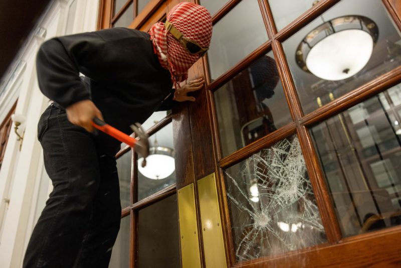 NEW YORK, NEW YORK - APRIL 29: A demonstrator breaks the windows of the front door of the building in order to secure a chain around it to prevent authorities from entering on Tuesday, April 30, 2024 in New York City. Demonstrators from the pro-Palestine encampment on Columbia's Campus barricade themselves inside Hamilton Hall, an academic building which has been occupied in past student movements,. Pro-Palestinian demonstrators marched around the 