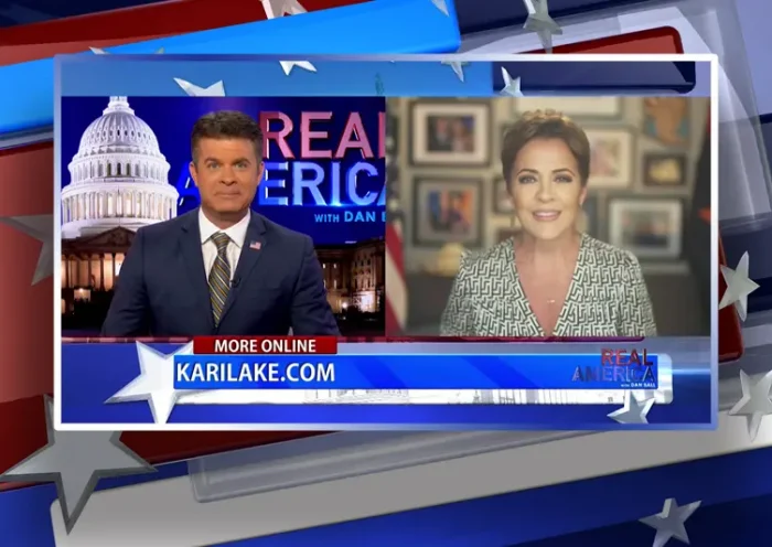 Video still from Real America on One America News Network showing a split screen of the host on the left side, and on the right side is the guest, Kari Lake.