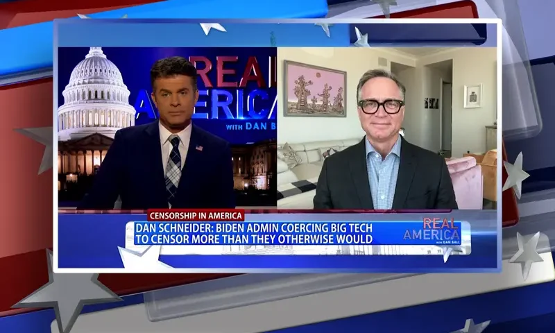 Video still from Real America on One America News Network showing a split screen of the host on the left side, and on the right side is the guest, Dan Schneider.