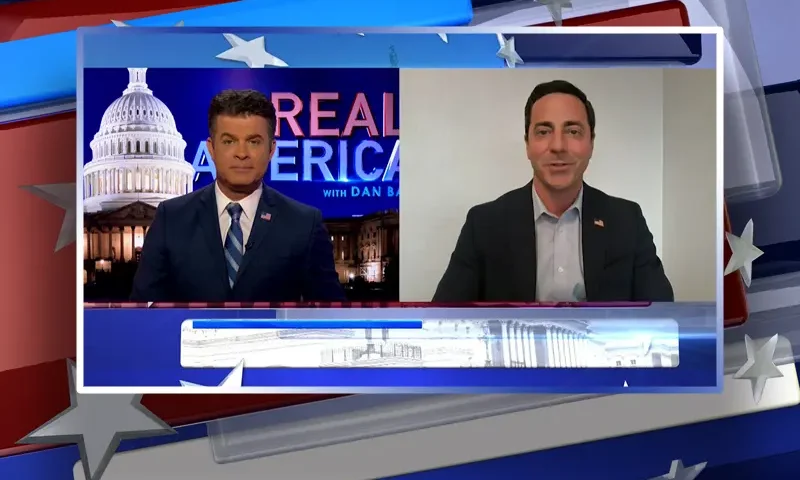 Video still from Real America on One America News Network showing a split screen of the host on the left side, and on the right side is the guest, Trent Staggs.