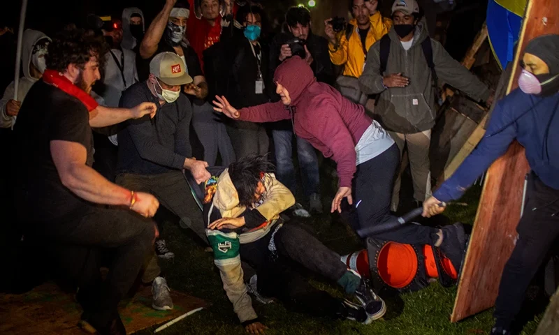 Demonstrators clash at an encampment at UCLA early Wednesday, May 1, 2024, in Los Angeles. Dueling groups of protesters have clashed at the University of California, Los Angeles, grappling in fistfights and shoving, kicking and using sticks to beat one another. (AP Photo/Ethan Swope)