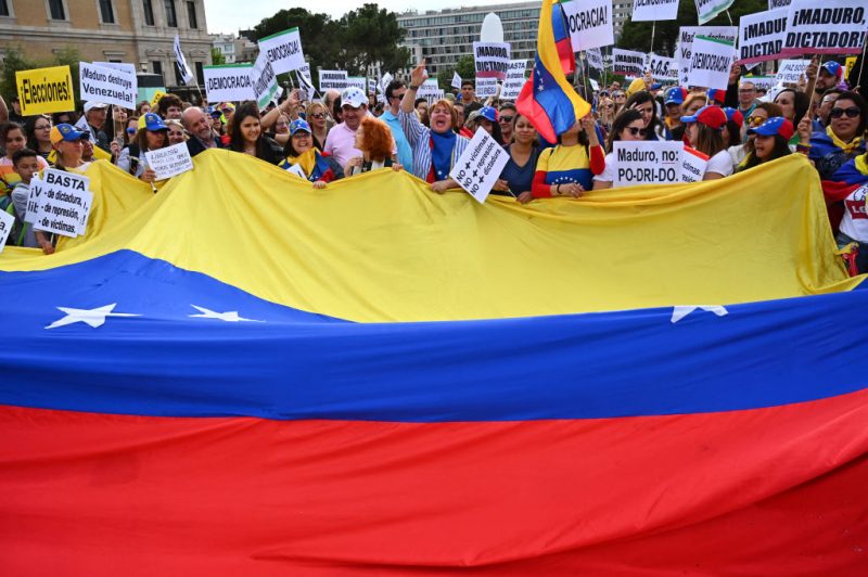 Venezuelans living in Spain hold a giant Venezuelan flag as they protest in support of the Venezuelan opposition during a demonstration in Madrid on May 1, 2019. Hundreds of Venezuelans rallied in central Madrid in support of their country's self-proclaimed leader Juan Guaido, as riots broke out in faraway Caracas. (Photo by GABRIEL BOUYS / AFP) (Photo by GABRIEL BOUYS/AFP via Getty Images)