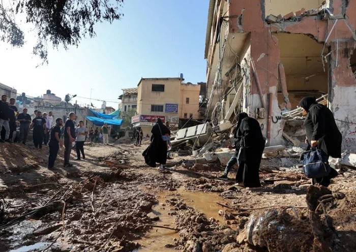 Palestinians walk next to a building damaged during a raid by Israeli troops at the Nur Shams refugee camp near the northern city of Tulkarm in the occupied West Bank on October 20, 2023. At least 81 Palestinians have been killed by Israeli troops or settlers in the West Bank since the Gaza conflict erupted on October 7, according to ministry figures. (Photo by Zain JAAFAR / AFP) (Photo by ZAIN JAAFAR/AFP via Getty Images)