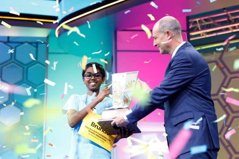NATIONAL HARBOR, MARYLAND - MAY 30: Twelve-year-old Bruhat Soma, of Tampa, Florida, is handed the Scripps Cup by E. W. Scripps Company CEO Adam Symson after winning the 2024 Scripps National Spelling Bee at the Gaylord National Resort and Convention Center on May 30, 2024 in National Harbor, Maryland. Soma spelled 29 words correctly in a tiebreaker spell-off to win the competition. The competition began with 245 spellers from around the world. (Photo by Anna Moneymaker/Getty Images)