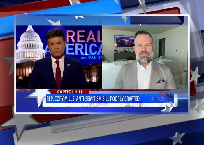 Video still from Real America on One America News Network showing a split screen of the host on the left side, and on the right side is the guest, Cory Mills.