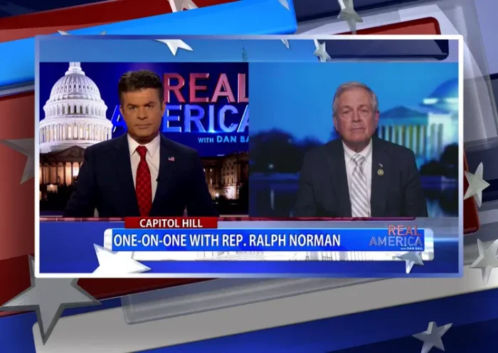 Video still from Real America on One America News Network showing a split screen of the host on the left side, and on the right side is the guest, Rep. Ralph Norman.